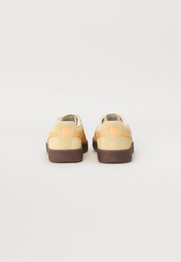 Baskets en daim jaune et marron avec une semelle en caoutchouc, présentant une texture lisse, un talon plat et un design minimaliste.