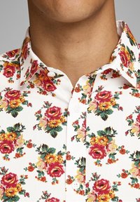 Biała koszula na guziki z kolorowym, kwiatowym wzorem w odcieniach czerwieni, żółci i zieleni na jasnym tle. Miękka faktura materiału.