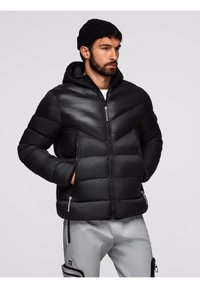 Giacca a vento nera con cappuccio, caratterizzata da un design a chevron, tasche con zip e una texture liscia e lucida. Coulisse regolabile sul cappuccio.