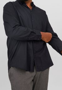 Camisa negra de manga larga, confeccionada en una tela suave, con un corte relajado y un dobladillo curvado. Cuenta con collla y cierre de botones.