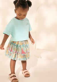 Tricou bleu deschis din bumbac cu grafică "Princesses Disney" asortat cu o fustă plisată cu ilustrații colorate cu prințese. Sandale roz.