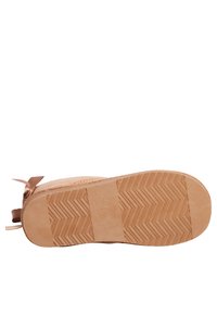Suela de zapatilla en un beige claro con un patrón de agarre texturizado y bordes suaves, presentando un acento decorativo de lazo en el lateral.