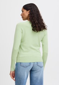Maglione lavorato a maglia verde chiaro con maniche lunghe, design aderente, orlo a coste e collo a girocollo. Abbinato a jeans blu a vita alta.