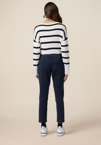 Randig vit och marinblå långärmad topp, mörk marinblå byxor och vita sneakers med silverdetaljer. Bakifrån syns den avslappnade passformen och stilen.
