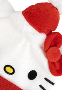 Cappello bianco con accenti rossi, caratterizzato da un design di personaggio. Texture morbida con elementi in peluche, orecchie rotonde e dettaglio a fiocco. Caratteristiche ricamate in nero e giallo.