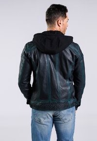 Černá kožená bunda s připevněnou černou mikinou, zdobená zelenými akcenty a prošívanou spodní zadní částí. Nosit s modrými džíny.