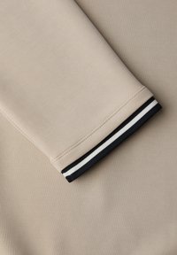 Beiger Stoffärmel mit einem schwarz-weiß gestreiften Manschettendetail auf einem passenden beigen Hintergrund.