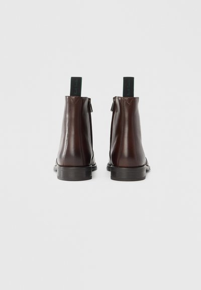 Braune Leder-Stiefeletten mit glatter Textur, runden Zehen und einer dicken Gummisohle. Verfügen über einen grünen Zuglasche und seitliche Reißverschlüsse.