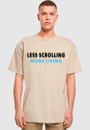 Beige cotton t-shirt with short sleeves featuring black and blue text "LESS SCROLLING MORE LIVING." Relaxed fit and soft texture.