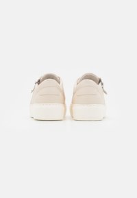 Et par beige slip-on sneakers med tykke hvide såler vist fra ryggen mod en simpel hvid baggrund.