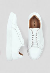 Białe skórzane sneakersy o gładkiej fakturze, okrągłym nosku i sześciu oczkach. Zawierają brązową wkładkę i subtelne logo marki wewnątrz.