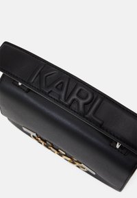 Borsa a mano nera in pelle con il nome "KARL" in rilievo sulla tracolla, dotata di un dettaglio in catena dorata e superficie liscia. Forma rettangolare.