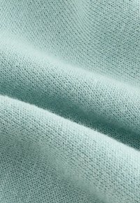 Hellblau-grüner Stoff mit einem weichen, strukturierten Strick. Sichtbare Nähte erzeugen ein glattes, warmes Aussehen, welches sich gut für Bekleidung oder Accessoires eignet.