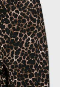 Gros plan sur un tissu à imprimé léopard marron et noir avec une couture de poche visible sur le côté droit.