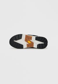 Black, white, and brown rubber sneaker sole with deep grooves and textured tread designed for grip on flat white background.