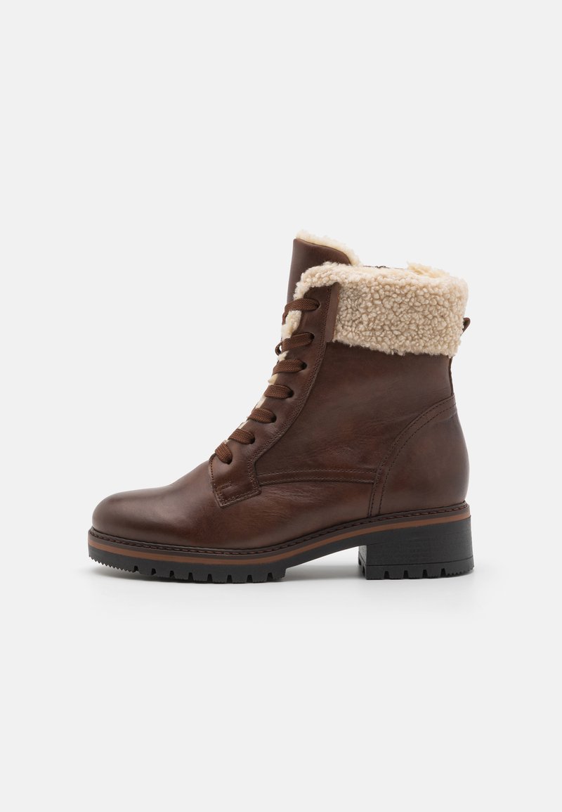 Botín de cuero marrón hasta el tobillo con parte delantera con cordones, cuello forrado de piel y suela de goma texturizada. Cuenta con un tacón grueso para mayor soporte.