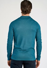 Miękki, turkusowy sweter z dzianiny, z kołnierzykiem polo, prążkowanymi mankietami i dołem. Gładka struktura z dopasowanym krojem.