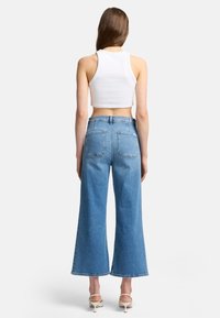 Lyseblå høytlivete flared jeans med en klassisk denimstruktur, som har to baklommer og glidelås. Avkortet hvit tank top.