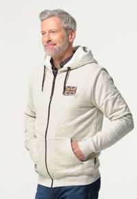 Lichtgrijze rits hoodie met een capuchon, voorzien van een Union Jack-patch en bruine trekkoorden. Het heeft voorzakken en geribbelde manchetten.