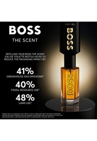 Bottiglia di profumo Boss The Scent ricaricata con un contenitore nero, evidenziando la riduzione dell'impatto dell'imballaggio: 41% emissioni, 40% risorse, 48% uso del suolo.