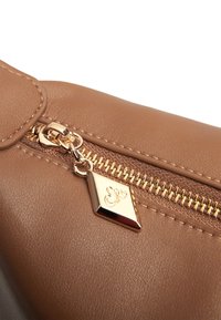 Borsa in finta pelle marrone in primo piano con zip dorata, minuteria decorativa e superficie texture. La zip è dotata di un ciondolo a forma di diamante.
