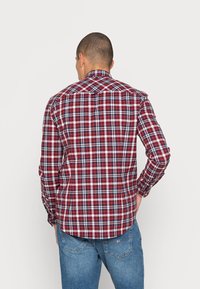 Röd och marinblå rutmönstrad skjorta med knappar, långa ärmar och en rundad fåll, med standardkrage och detalj på ryggen.