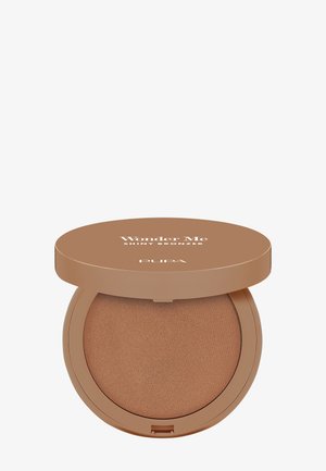 Puder brązujący w okrągłym, kompaktowym opakowaniu z błyszczącą, jasnobrązową pokrywką, na której znajduje się napis "Wonder Me Shiny Bronzer" oraz gładką, brązową powierzchnią.