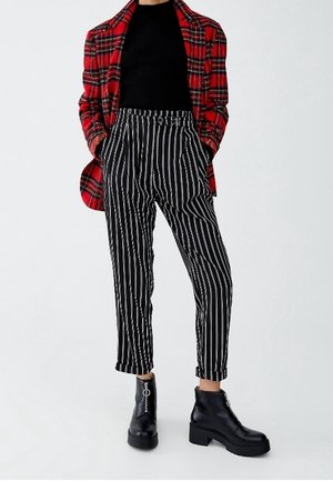 Rødrutet blazer, sort ribbet top, bukser med sort-hvide striber og sorte ankelstøvler med chunky hæle. Skræddersyet pasform med synlige lommer.