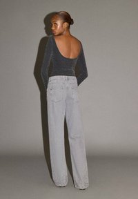 Črn bodi z dolgimi rokavi in nizkim hrbtom, kombiniran z svetlo sivimi širokimi trapericami visoko v pasu, ki imajo subtilne izreze.