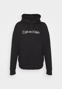 Black hooded sweatshirt made of cotton blend. Features a front kangaroo pocket and white "Calvin Klein" logo printed on the chest.