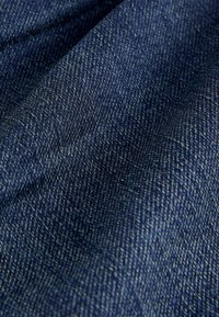 Tumedat sinised denimkangad, millel on tekstuuriga herringbone muster ja kerge venivus, näidates heledate ja tumedate niitide kudumist.
