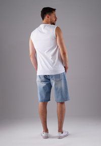White sleeveless tank top, light blue denim shorts, and white sneakers. The shorts feature back pockets and a faded texture.