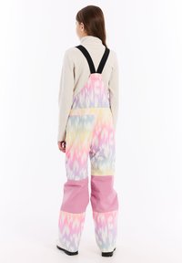 Pestré lyžiarske overal s batikovaným vzorom v pastelových odtieňoch, s pevným ružovým dolným dielom a čiernymi nastaviteľnými popruhmi.