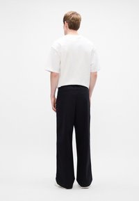 Tricou alb din bumbac cu mâneci scurte, asociat cu pantaloni negri cu croi larg. Outfitul este văzut din spate, arătând detalii de design minime.