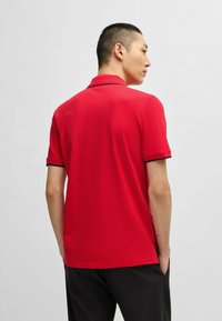 Rød polo skjorte med ensfarvet design, korte ærmer med sort kant og klassisk krave. Glat tekstur og tætsiddende pasform.