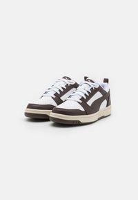 Brune og hvite sneakers med perforert tå, hvite snørebånd og en tan såle. Har et slankt design og sideaksenter.