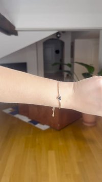 Auksinės spalvos apyrankė su pailgintomis metalinėmis grandinėlėmis, maža juoda širdelės sagė ir krintantis karoliukas. Lygi tekstūra ir paprastas dizainas.