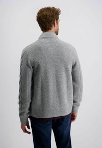 Grauer Strickcardigan mit einem Schalkragen, gerippten Ärmeln und einem strukturierten Obermaterial. Sichtbare Schichtung über einem dunklen Shirt und blauen Jeans.