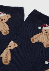 Marineblå sokker med et strikket design, der har brune teddy-bjørne iført røde og hvide julesokker. Blød tekstur med detaljeret mønstring.