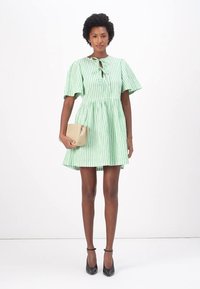 Vestido riscado em verde e branco com mangas curtas, gola com laço e saia evasê. Acompanhado por uma clutch bege e sapatos de salto pretos.