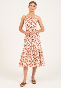 Robe midi florale avec décolleté carré, motif fleurs rouges et vertes sur tissu crème, ourlet à volants en couches, associée à des sandales marron.