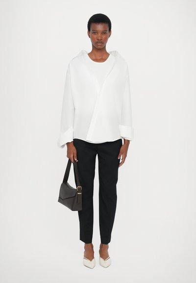 White oversized button-up shirt, black tailored pants, beige pointed-toe shoes, and a small brown handbag. Smooth fabric, simple design.