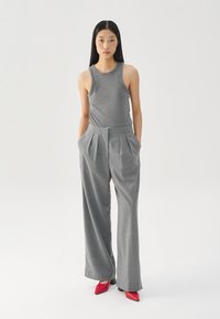 Gray ribbed tank top paired with loose-fitting gray pleated trousers. Notable red pointed-toe heels complete the outfit.