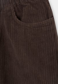 Gros plan sur la poche d’un pantalon en velours côtelé marron foncé avec texture striée verticale et taille élastique.