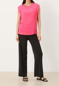 Růžový top bez rukávů s kulatým výstřihem, spárovaný s volnými černými kalhotami a plochými černými sandály. Hladký materiál a uvolněný střih.