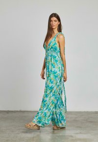 Sukienka maxi w zwiewnym, turkusowym materiale z wzorem tie-dye, z głębokim dekoltem w kształcie litery V i plecionymi ramiączkami, w połączeniu z ozdobnymi sandałami na platformie.