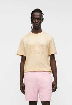 Lichtgele katoenen T-shirt met een reliëf "LACOSTE"-logo en krokodillenontwerp, gecombineerd met zachtroze gestructureerde shorts.