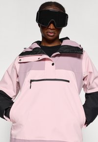 Roosa ja hall suusajope pooltõmblukuga esiosas, reguleeritava kapuutsiga ja lukuga rinnaotsaga. Mustad detailid varrukatel ja äärel.