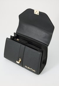 Bolso de cuero negro con herrajes dorados, forma estructurada y cierre superior. El interior cuenta con compartimentos y una sección con cremallera.