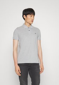 Polo gris de mezcla de algodón, con mangas cortas, un collar y tres botones negros; presenta un pequeño logo en el pecho izquierdo.